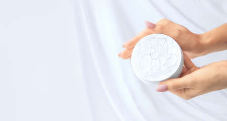Hands with an open jar of cream on a white silk background. Copy spaceの写真素材