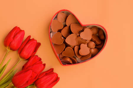 Holiday gift. Heart shaped box with chocolates and red tulips on a brown background.の写真素材