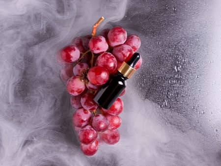Black bottle with a dropper on a bunch of grapes in the smoke. Black backgroundの写真素材