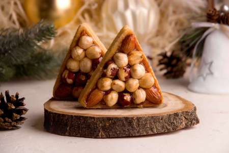 The concept of New Year's cookie recipes. Triangular sweet cookies with nuts on the background of a Christmas treeの写真素材