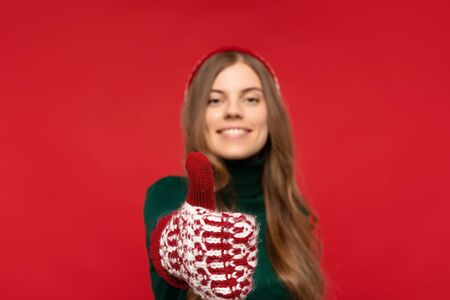 selective focus of woman in winter hat showing thumb up isolated on red background. Christmas conceptの写真素材