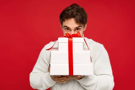 man in white sweater with obscure face holding Christmas presents isolated on red background. Christmas conceptの写真素材