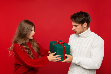 angry young couple holding Christmas presents isolated on red background. Christmas conceptの写真素材