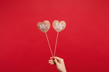 cropped view of woman holding decorative hearts on sticks with mrs and mr lettering isolated on red backgroundの写真素材