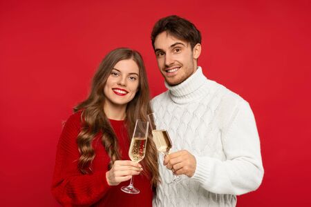 smiling couple clinking champagne glasses and looking at camera isolated on red background. Christmas conceptの写真素材