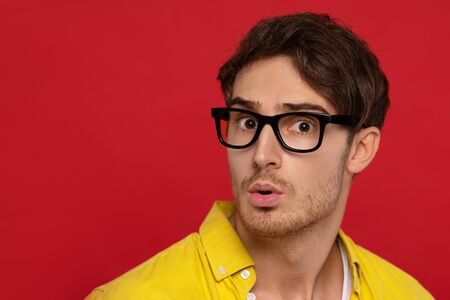 shocked man in yellow shirt and glasses isolated on red background. Face expressions conceptの写真素材