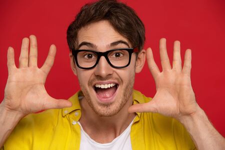 excited man in yellow shirt and glasses showing hands with open mouth, has joyful face expression,...