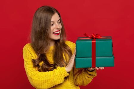 happy beautiful girl looking at Christmas presents isolated on red background, shows white teeth. Christmas conceptの写真素材