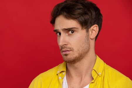 worried man in yellow shirt looking at camera isolated on red background. Face expressions conceptの写真素材