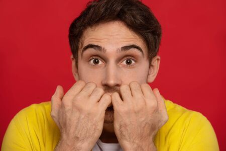scared handsome man in yellow shirt with hands near face isolated on red background