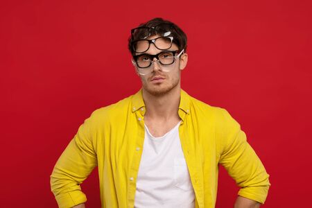 serious funny handsome man in yellow shirt with many eyeglasses on face isolated on red backgroundの写真素材