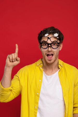 funny handsome man with open mouth in yellow shirt with many eyeglasses on face showing idea gesture isolated on red backgroundの写真素材
