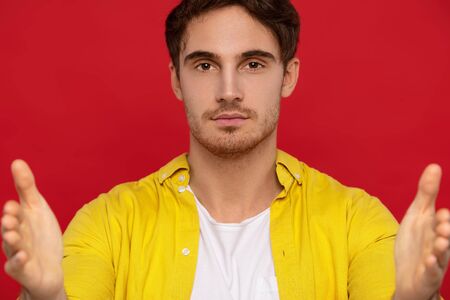 selective focus of handsome man in yellow shirt pointing with hands at camera isolated on red backgroundの写真素材