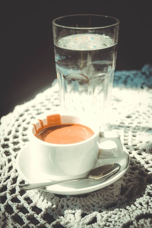 White mug of hot chocolate and a glass of water from a transparent glass on a table, a bright light, the filterの写真素材