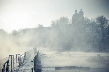 silhouette of a man who goes across the bridge over the river with condensate winter frosty morningの写真素材
