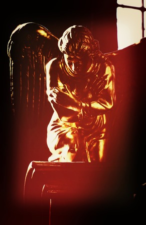 golden figure of an angel with wings, sitting on his knees on a black backgroundの写真素材