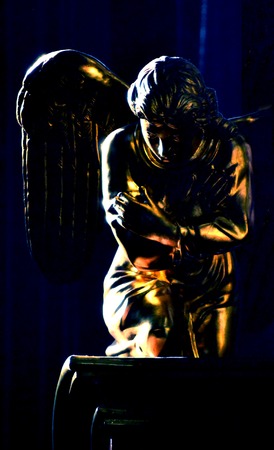 golden figure of an angel with wings, sitting on his knees on a black backgroundの写真素材