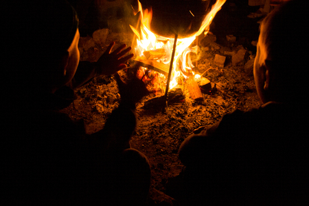 children sit around the campfire at night and warm handsの写真素材