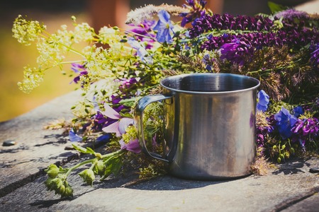 Metal mug on a table with flowers lying on itの写真素材