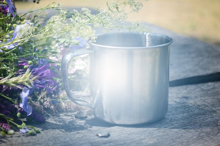 Metal mug on a table with beautiful blooming flowers, filter,の写真素材