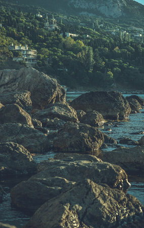 large stones in the water on the beach near the mountains, wooded with houses, filterの写真素材