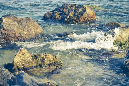 stones in clear water with white foam near the shoreの写真素材