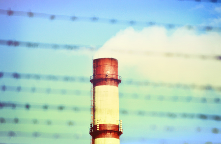 top of the pipe with smoke through the barbed wire against the blue skyの写真素材