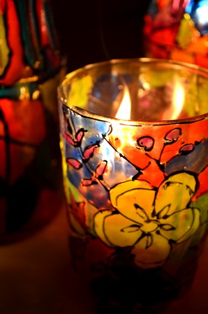 glass candle holder painted stained glass paints with a burning candle insideの写真素材