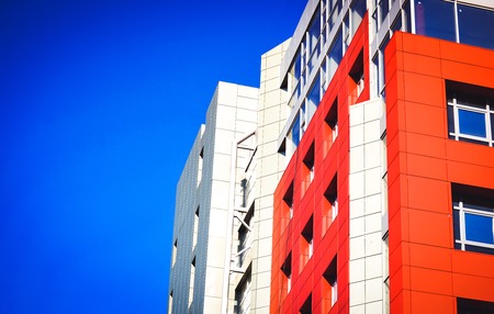 Part of the facade of a modern building with red walls, square windows, the blue mirrored glass....