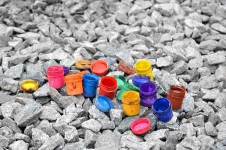 small jars from under paint of different colors on gray pebblesの写真素材