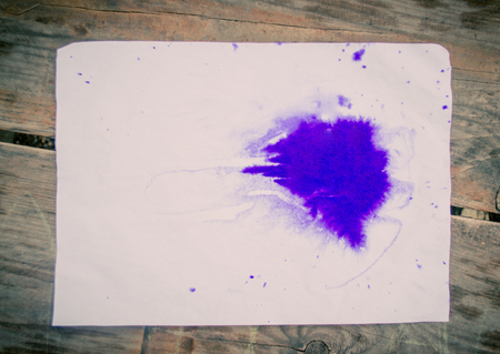 Blank sheet owhite paper purple blot lies. Blue blot of ink on a sheet of white paper on a wooden surface. Abstract base basis background backdrop. Space for textの写真素材