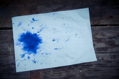 Blank sheet owhite paper purple blot lies. Blue blot of ink on a sheet of white paper on a wooden surface. Abstract base basis background backdrop. Space for textの写真素材