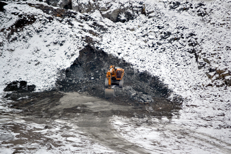 big huge yellow excavator in a granite quarry in winter. huge loading shovel bucket stands on a granite floor strewn with snow in his career on a winter dayの写真素材