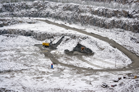 big huge yellow excavator in a granite quarry in winter. huge loading shovel bucket stands on a granite floor strewn with snow in his career on a winter dayの写真素材