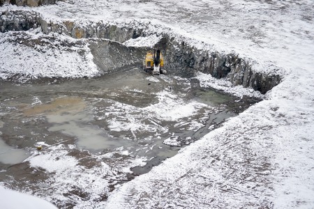 big huge yellow excavator in a granite quarry in winter. huge loading shovel bucket stands on a granite floor strewn with snow in his career on a winter dayの写真素材
