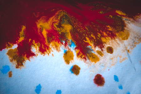 divorces and paint drips red, orange, yellow, blue blurred abstract background on a white paper background plane surface close-up macro with filter toning effectの写真素材