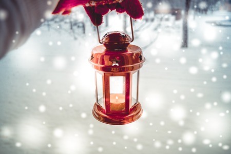 Holding in red glove a red candle lantern in the winter forest. Snow forest snowfall. Christmas Winter New Year background trembling flame Scenery. Fairy magic forest flashlightの写真素材