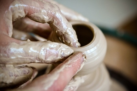 Girl sculpts in clay pot closeup. Modeling clay close-up. Caucasian man making vessel daytime of white clay in fast moving circle. Art, creativity. Ukraine, cultural traditions. Hobbiesの写真素材