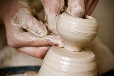 A man with his hands dub wall jug, which he sculpts out of clay on a circle. Create clay vessel. Modeling white-clay, shaping vessel. Caucasian man making vessel Cclay in circle.の写真素材