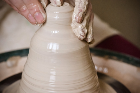 A man with his hands dub wall jug, which he sculpts out of clay on a circle. Create clay vessel. Modeling white-clay, shaping vessel. Caucasian man making vessel Cclay in circle.の写真素材