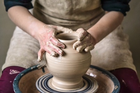 Girl sculpts in clay pot closeup. Modeling clay close-up. Caucasian man making vessel daytime of white clay in fast moving circle. Art, creativity. Ukraine, cultural traditions. Hobbiesの写真素材