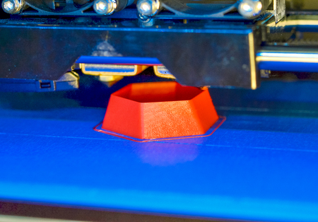 3d printer printing red faceted geometric shapes on a blue background close-up. Bright contrast image automatic three dimensional 3d printer performs plastic modeling in laboratory.の写真素材