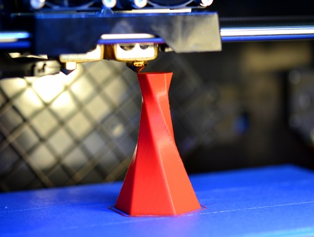 3D printer printing isolated volume triangular object red color on the basis of blue and black background close-up. Modern 3d printing technologyの写真素材