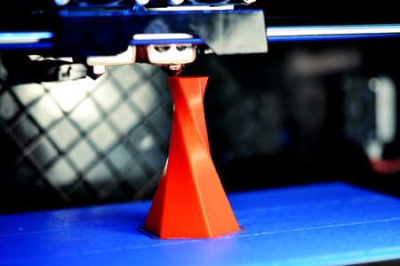 3D printer printing isolated volume triangular object red color on the basis of blue and black...