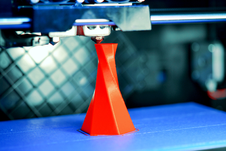 3D printer printing isolated volume triangular object red color on the basis of blue and black background close-up. Modern 3d printing technologyの写真素材
