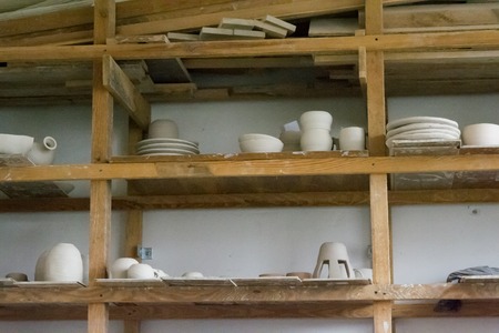 Bright pottery. Many white, not painted clay pottery standing on wooden shelvesの写真素材