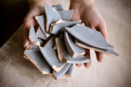 In hand debris or smithereens. Ware splinters in hands closeup. Caucasian man holds in the hands of the debris or fragments of pottery broken plateの写真素材
