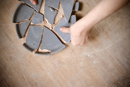 Person split a clay plate on the table close-up. Top view
