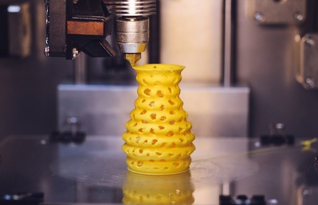 3D printer prints from the plastic figure closeup. 3D printer makes yellow model close-up on gray flat surfaceの写真素材