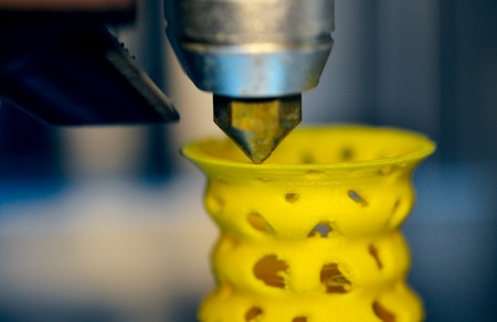 3D printer prints from the plastic figure closeup. 3D printer makes yellow model close-up on gray flat surfaceの写真素材